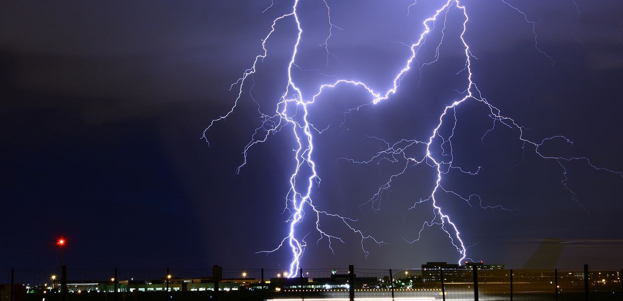 Zwei helle Blitze schlagen bei Nacht am Rand einer beleuchteten Stadt ein