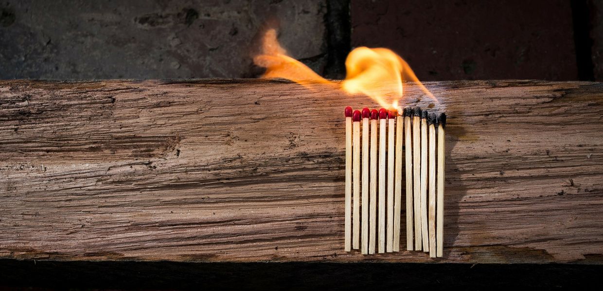 Eine Reihe nebeneinander aufgestellter Streichhölzer auf einem Holzbalken, von denen ein Teil bereits abgebrannt ist
