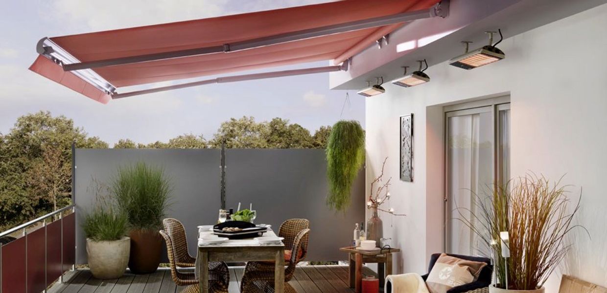 Überdachte Terrasse mit ausgefahrener Markise und elektrischen Heizstrahlern an der Hauswand über dem Esstisch