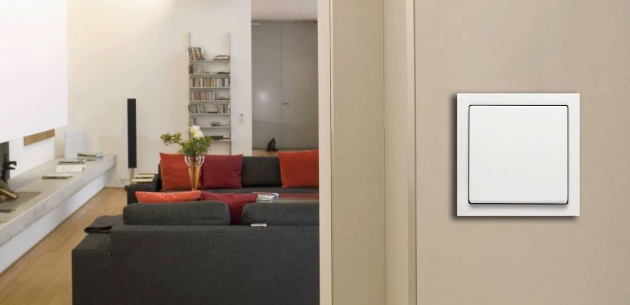 Weißer Wippschalter an einer Wand, dahinter der Blick in einen Wohnraum mit Sofa