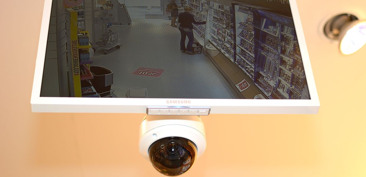 Deckenkamera unter einem Monitor, auf dem die Aufnahme eines Verkaufsraums zu sehen ist